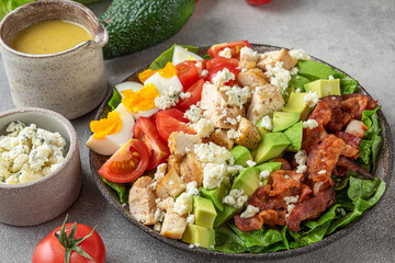 Healthy cobb salad with chicken, avocado, bacon, blue cheese, tomato and eggs on gray background....