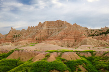 mountains in badlands national park. There is a lot of green grass growing in the foreground. The...