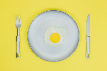 fried egg in gray plate and gray fork gray knife on yellow background.