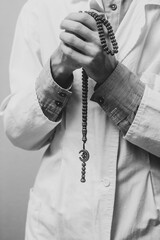 A young man in a white robe raised his hands up and prayed with a Muslim rosary. Medical gloves. Doctor praying. A Muslim makes dua. Black and white photo.