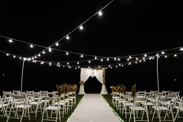 beautiful night stage for the wedding ceremony. wedding wooden arch. stylish wedding decor. chairs for the wedding ceremony. decorative bulbs illuminate the site. empty wedding venue