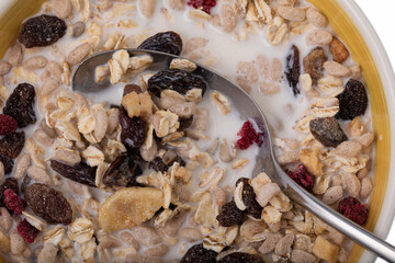 Breakfast oatmeal with nuts and dried fruits in yellow bowl with milk on white background