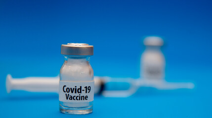 Vaccine for Covid 19 and a medical needle filled with vaccine on a blue background