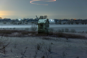 Colored lines over an old mill in a snowy field at night. Starry sky. Light graffiti