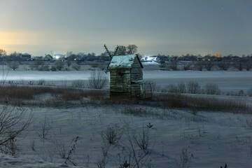 Old mill in a snowy field at night. Starry sky.