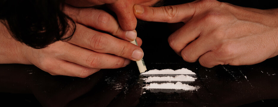 Drug addict man snorting cocaine powder with rolled dollar banknote. Narcotics concept. Close-up macro shot. Panoramic shot. Panorama banner. High resolution sharp photo.