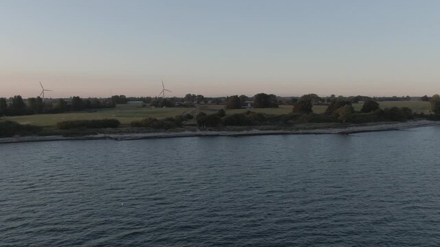 Aerial view of the baltic coast beach in Marielyst, Denmark. Sunset with wind turbines on the horizon and gulls flying. Ungraded footage.