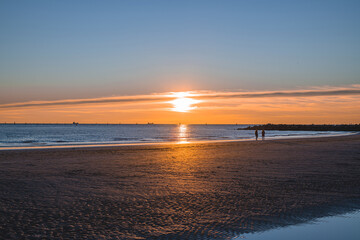 sunset at sea, sun on the same level with the sea and casual passers-by on the run