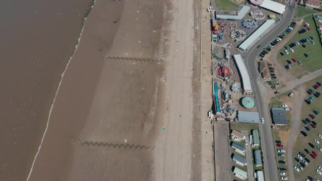 Aerial footage of the British seaside town of Hunstanton Norfolk, showing the coastal area and funfair fairground rides with people having fun and relaxing on the sandy beach in the summer time