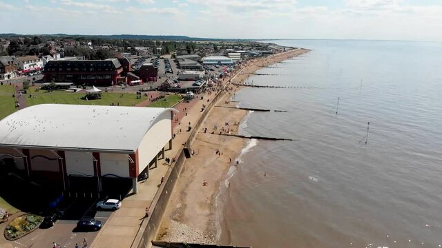 Aerial footage of the British seaside town of Hunstanton Norfolk, showing people and holiday makers on the sunny beach and in the ocean and the car park close to the sea front.
