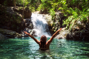 Beautiful girl with open arms near a waterfall in a tropical forest.