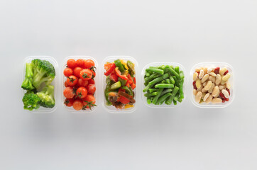 Frozen vegetables in plastic containers on white background.