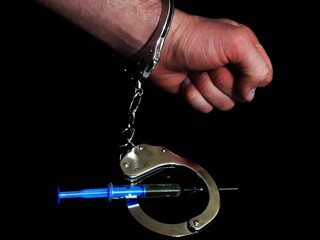 Handcuffed man and injection syringe, arrested drug dealer.
