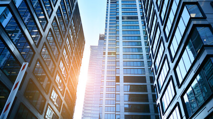 Fototapeta premium Bottom view of modern skyscrapers in business district against blue sky. Looking up at business buildings in downtown. Rising sun on the horizon.