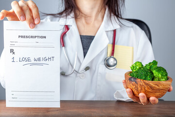 A caucasian female physician in white coat  is holding a prescription saying lose weight. She also...