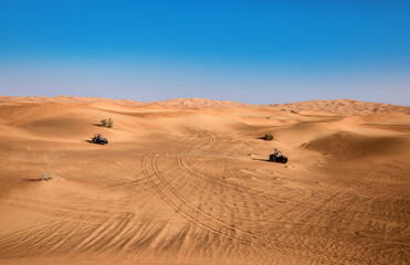 Beautiful Dubai desert landscape with plants and two riding quad buggy vehicles, sand with wheel...