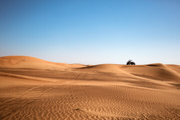 Fototapeta na wymiar Desert sandy minimalistic landscape with one black buggy quad bike far and wheels traces, safari tour at wild nature