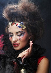 Young woman with creative makeup and and hairdo posing on dark background. Party time and halloween.