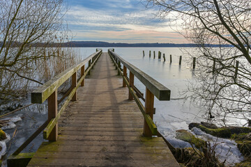 Wooden footbridge jetty on the frozen lake of Ratzeburg, last winter days in early spring, landscape in north Germany, copy space, selected focus