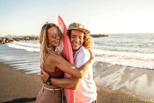 Happy surfer couple with surfboard having fun on the beach, smiling, spending time together. Sporty people. Real people emotions. Extreme surfing sport and youth relationship lifestyle concept