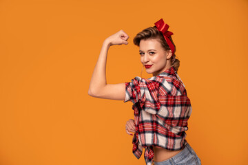 Studio shot of beautiful young woman with blond hair in pinup style clothes showing muscles to the camera, smiling.