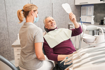 Man looking at mirror with smile in dentist’s office