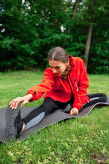 girl in the park sitting on a yoga mat doing stretching