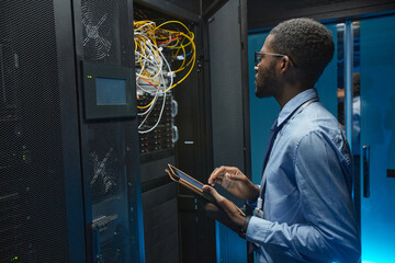 Side view portrait of African American man standing by server cabinet while working with...