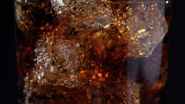 Fizzling cola in the glass. Closeup on black background