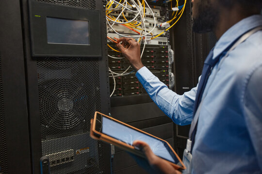 Cropper portrait of African American network engineer connecting cables in server cabinet while working with supercomputer in data center, copy space
