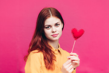 a woman on a pink background holds in her hand a red heart made of fabric Valentine's Day
