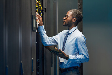 Graphic side view portrait of African American network engineer connecting cables in server cabinet while working with supercomputer in data center, copy space
