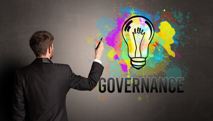 businessman drawing colorful light bulb with GOVERNANCE inscription on textured concrete wall, new business idea concept