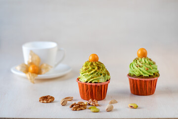 Two pancakes with pistachio cream and physalis sprinkled with nuts and a white tea cup and saucer are on the table.