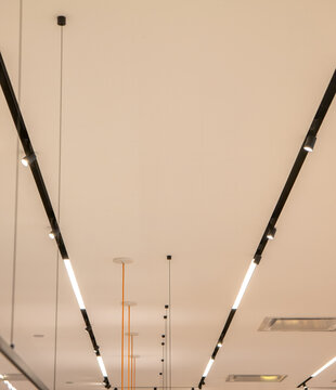 Modern Black And White Commercial Grade LED Lighting Fixtures And Support Bars Suspended From Taupe Ceiling Nobody