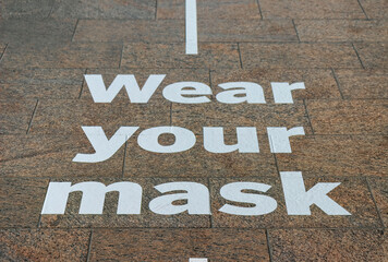 Signs painted in white on dark granite floors reminding people to wear masks due to COVID-19 nobody