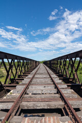 Abandoned iron railway bridge over a stream with a sky and clouds background