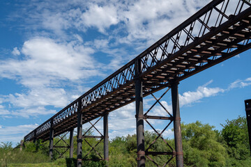 Abandoned iron railway bridge over a stream with a sky and clouds background