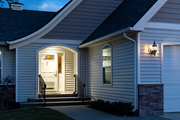 A home's front porch with a lockbox attached to the railing of the steps is illuminated at evening. - Powered by Adobe