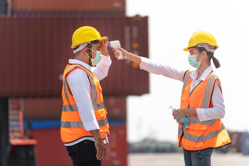 Factory woman worker in a face medical mask and safety dress used measures temperature at worker...