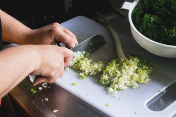 Las manos de una mujer picando cebolla de rama con un cuchillo sobre una tabla para picar