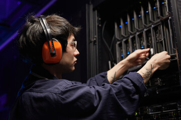 Side view portrait of tattooed young network engineer setting up servers in supercomputer data...