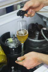 Las manos de un hombre sirviendo cerveza con una pistola en una copa de vidrio y de fondo los contenedores donde se guarda la cerveza