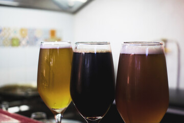 Detalle de tres copas de vidrio con cervezas de diferentes colores y sabores en una barra