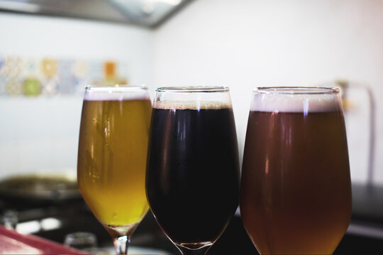 Detalle de tres copas de vidrio con cervezas de diferentes colores y sabores en una barra