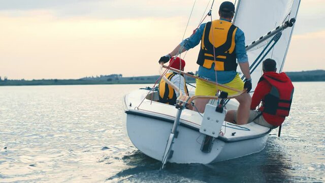 Three caucasian professional young sailor friends in life vests steering yacht together traveling by boat in beautiful sea.