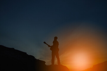 The silhouette of a man holding a guitar on a high hill