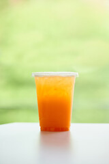 DISPOSABLE PLASTIC CUP DRINKS , plastic cup of tea for takeaway place on white table on green background. Close up and selective focus