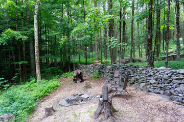 Two chairs and lanterns on a stump next to unlit campfire in the woods.