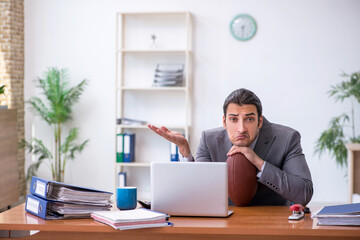 Naklejka premium Young male employee with rugby ball in the office